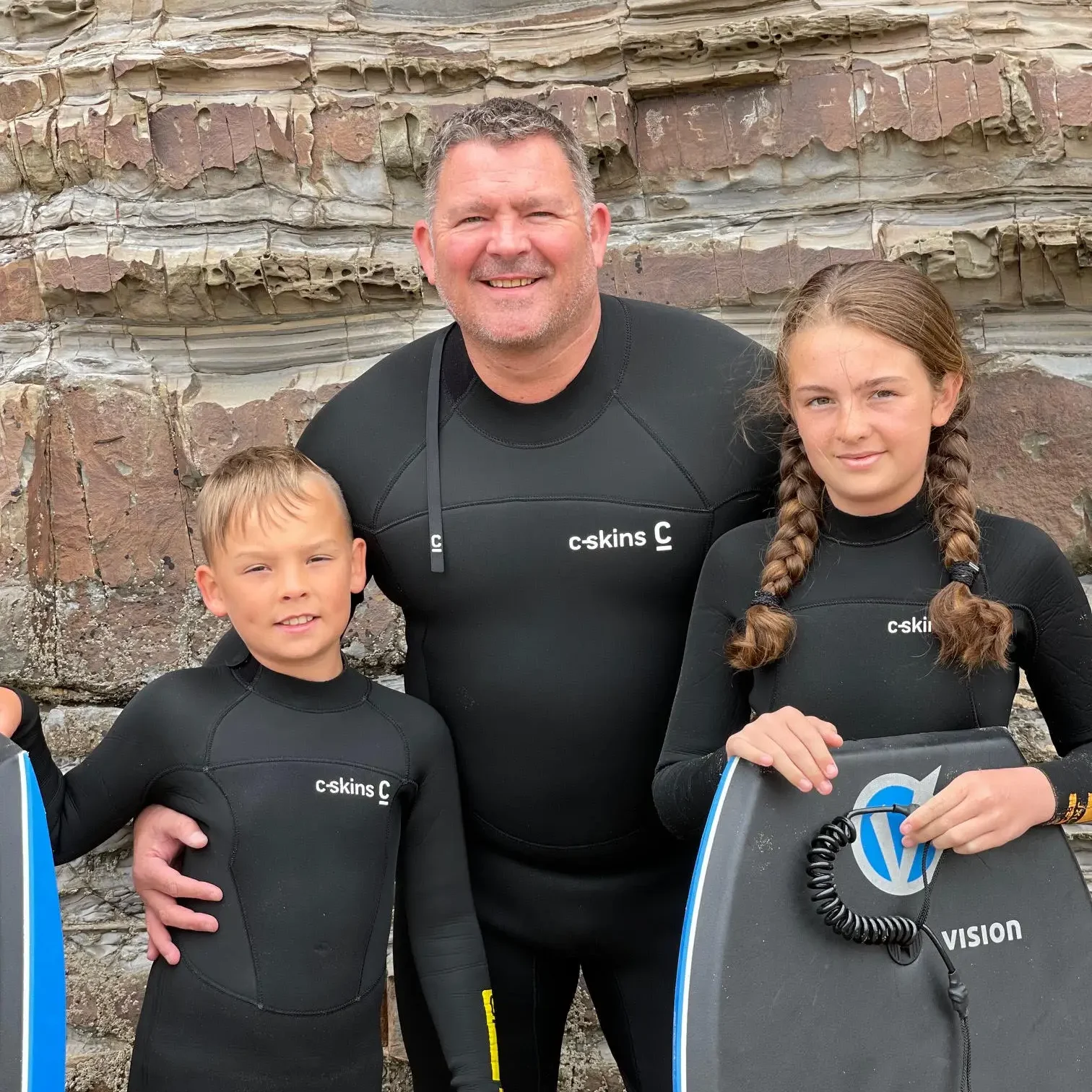 Nick and his children standing in surfing gear.